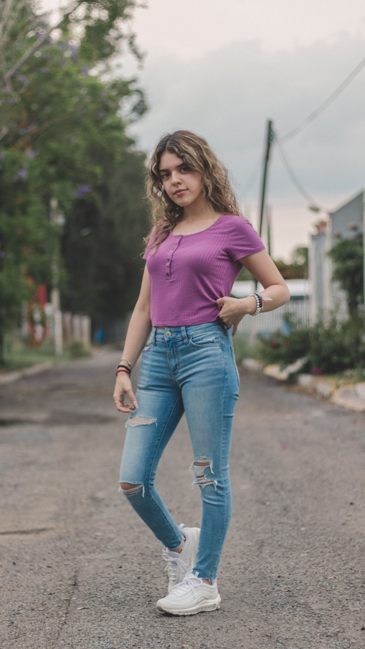 Woman styling high-waisted vintage denim jeans with a casual top on an urban sidewalk, representing timeless pre-owned denim silhouettes