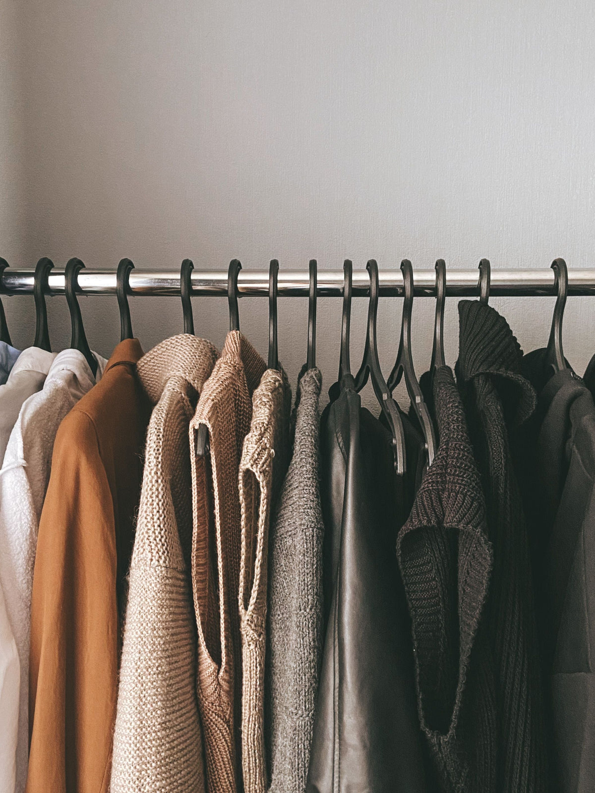 Curated capsule wardrobe of knitwear and sweaters hanging neatly in a closet