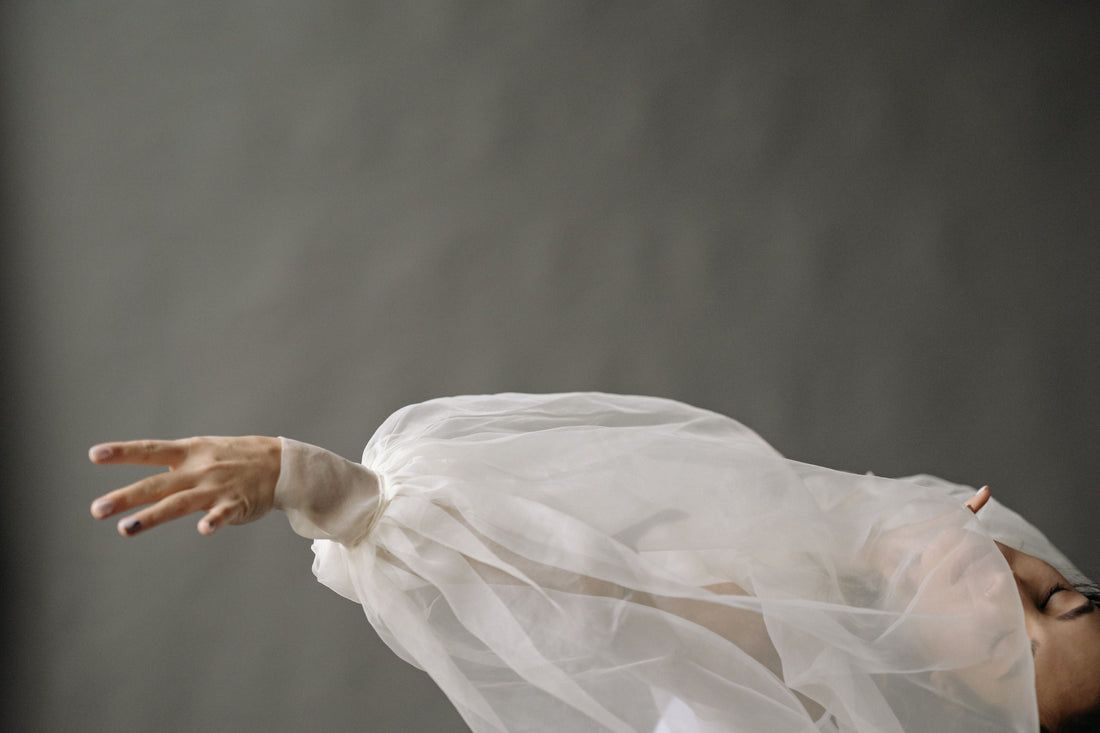 Elegant hand and arm draped in delicate white chiffon fabric, capturing the graceful movement central to CENT'ANNII's guide to caring for pre-owned chiffon