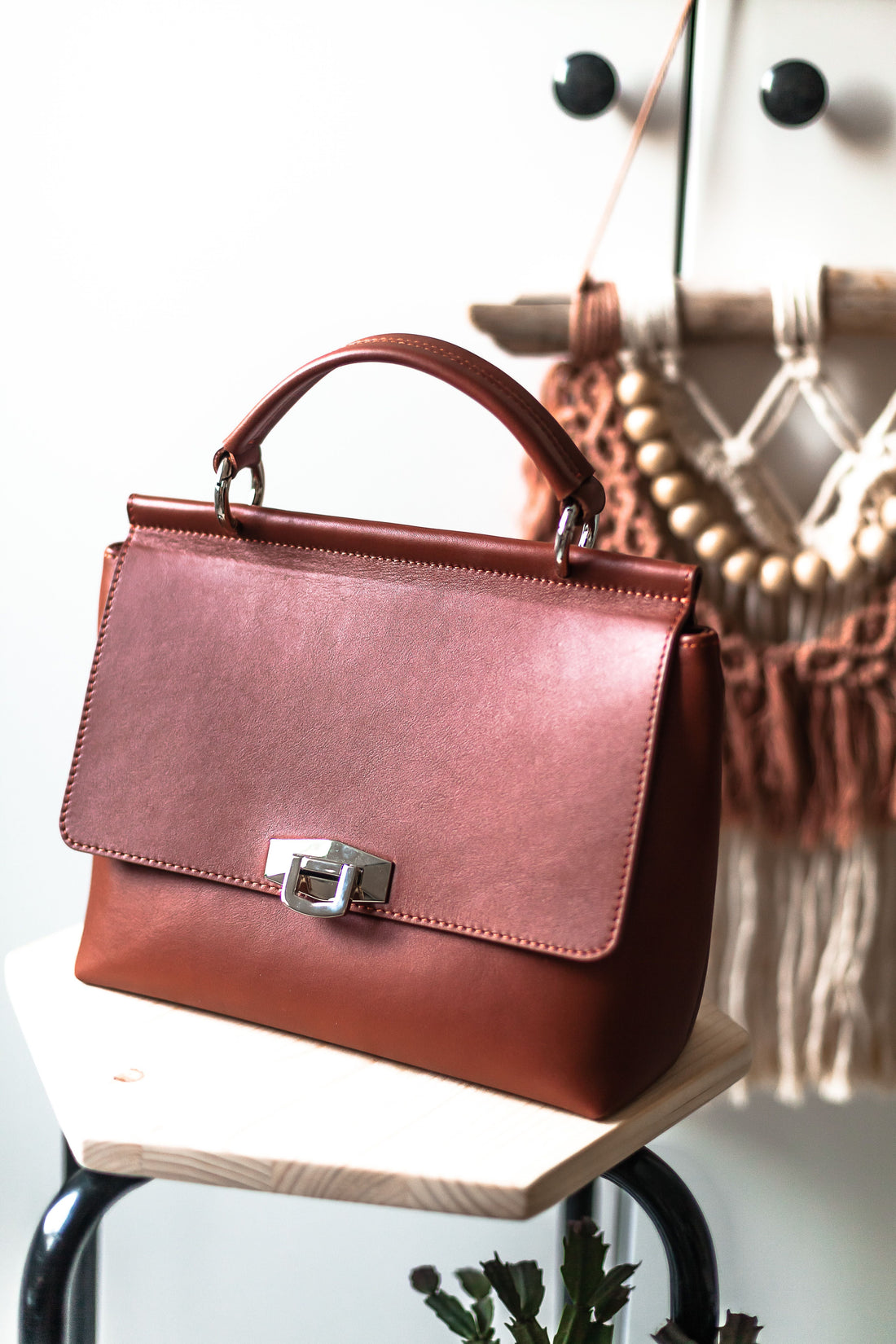 Brown leather Coach-style handbag styled on a stool in a bright, minimal room, representing the house's classic leather goods