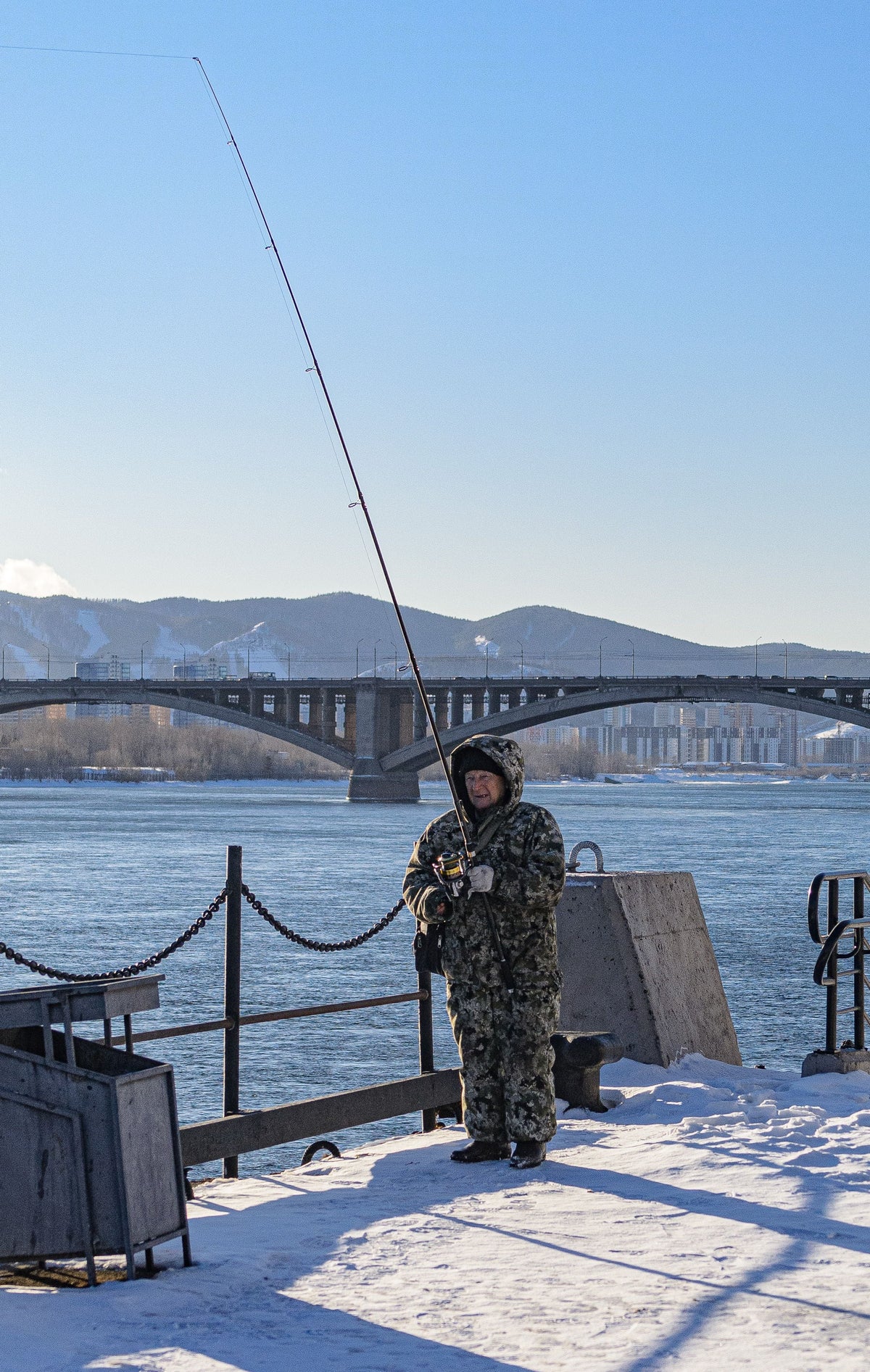 Man in an outdoor jacket fishing on a snowy riverbank, representing Columbia's outdoor heritage