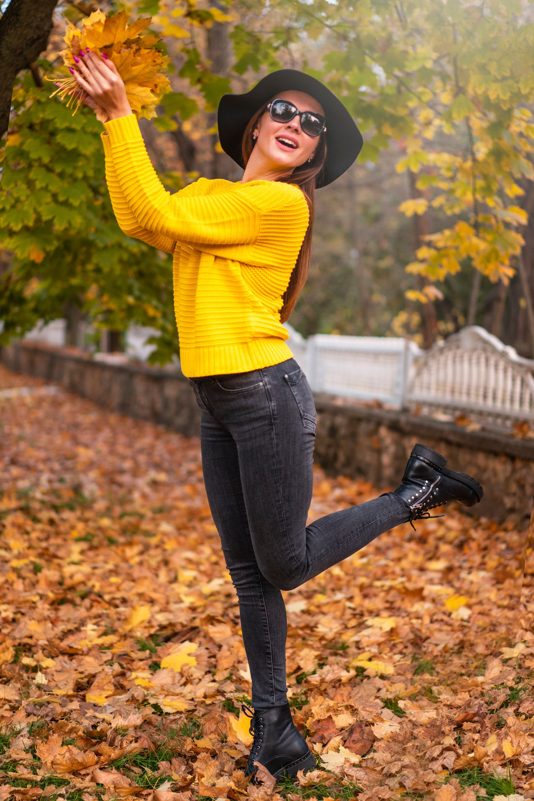 Woman layering a sweater over denim while standing among fallen autumn leaves, illustrating a fall layering outfit