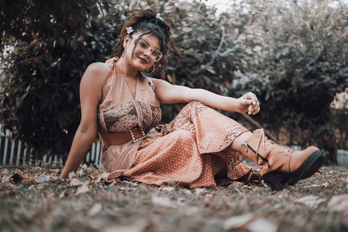Woman in a bohemian dress and layered accessories sitting in an autumn garden, evoking Free People's free-spirited style