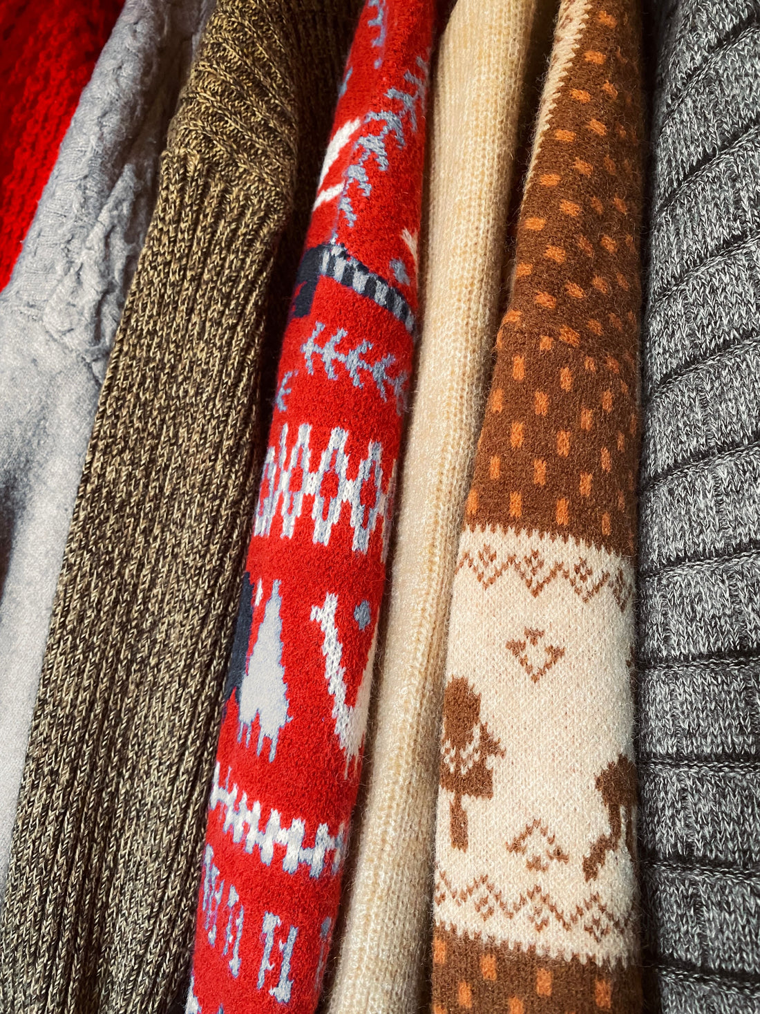 Collection of knitted wool sweaters in varied patterns hanging neatly on a rack
