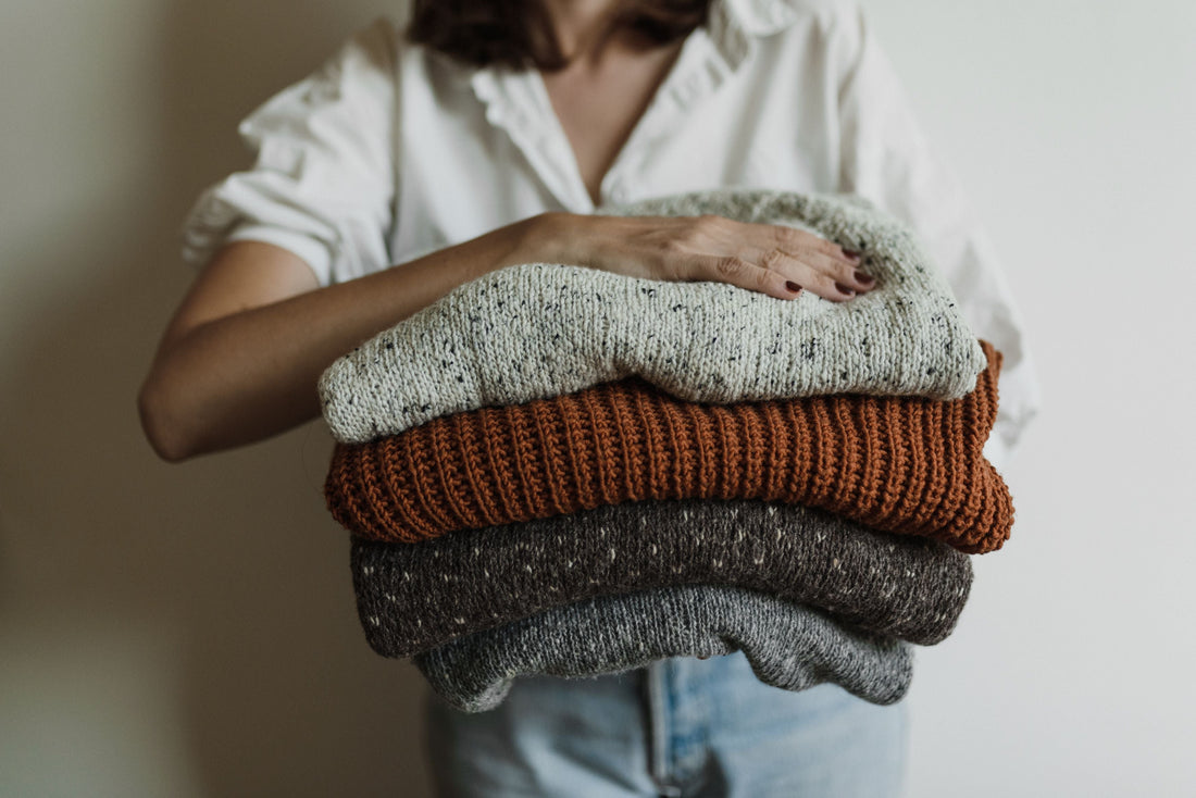 A stack of neutral-toned knit sweaters, representing the natural-fiber knitwear that benefits from proper pre-owned garment care