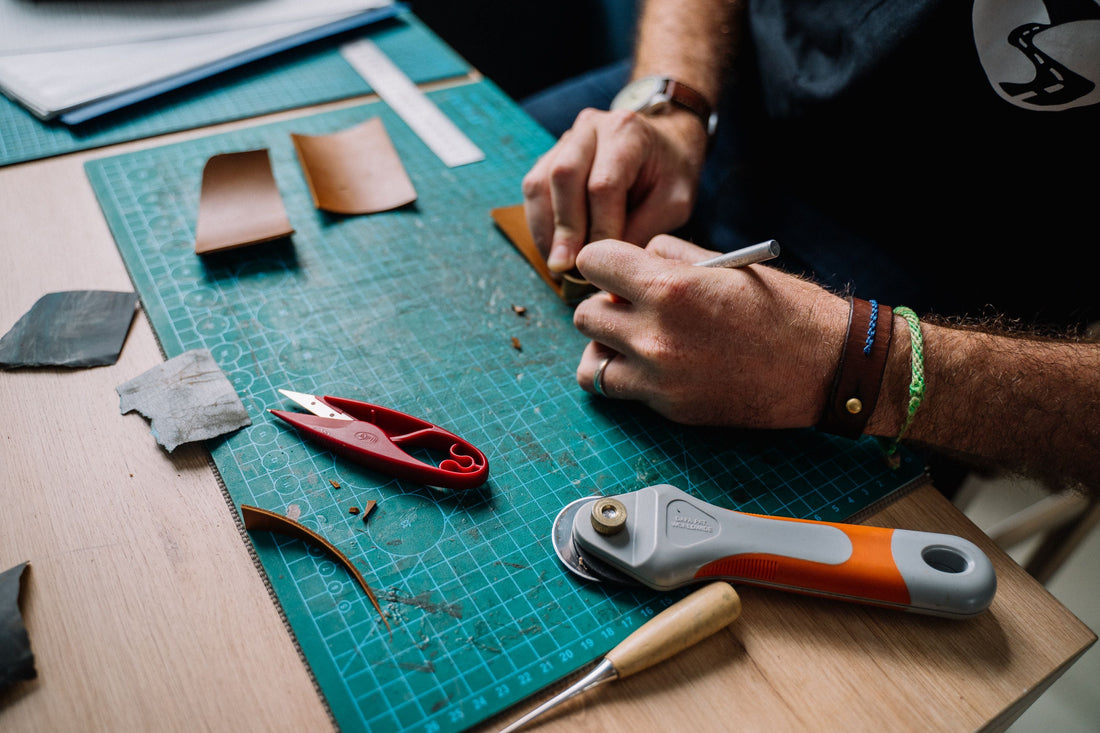 Close-up of a leather artisan hand-cutting and crafting a piece of leather on a workbench