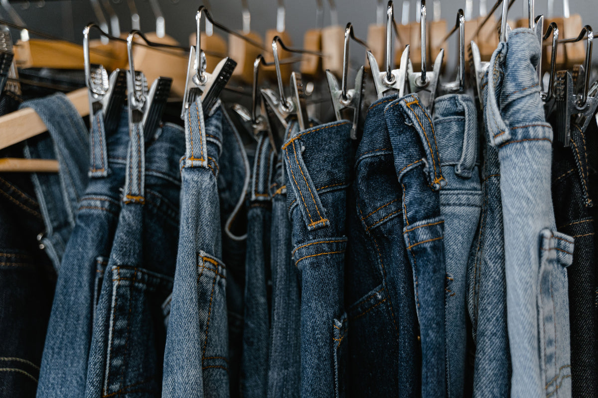 Close-up of an assortment of blue denim jeans hanging on a boutique clothing rack, representing the range of fits to compare when choosing between Levi's 501 and 505 styles