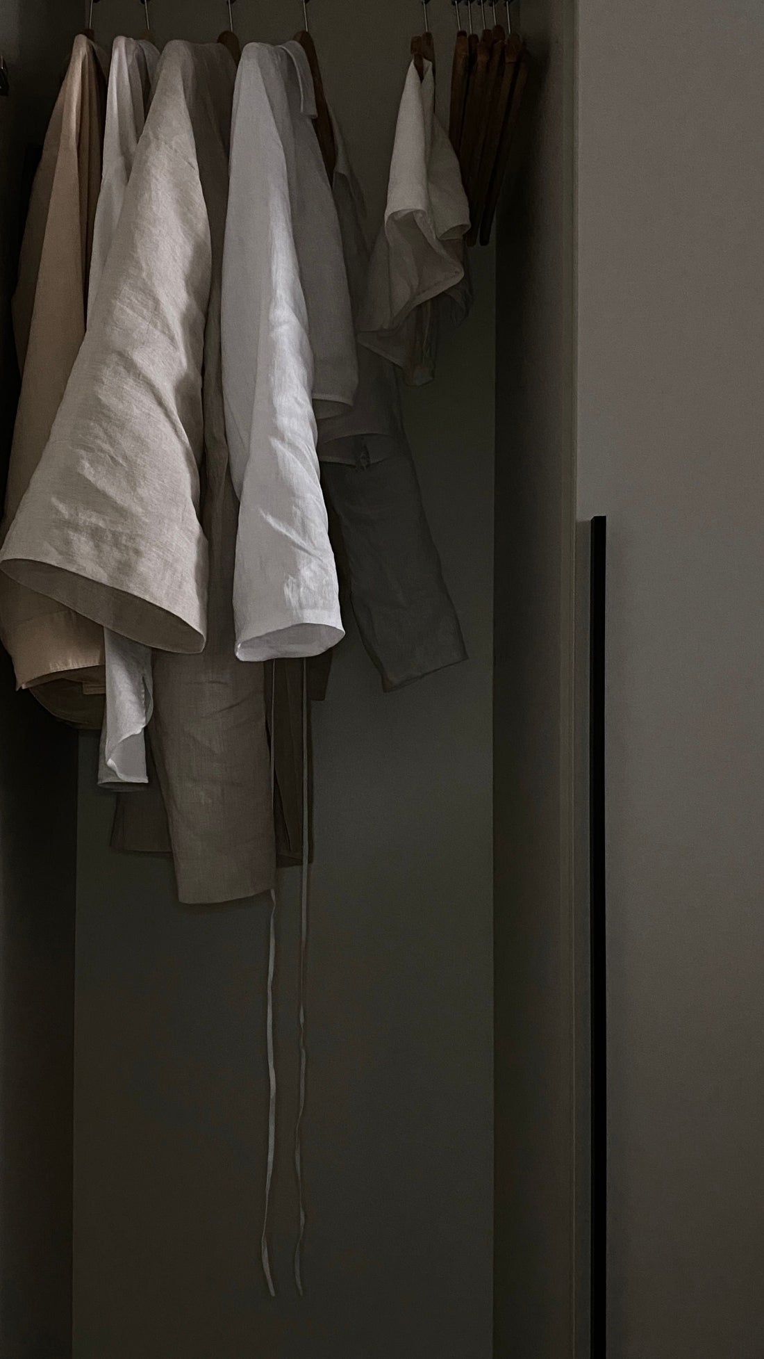 Pre-owned linen garments hanging on wooden hangers in soft natural light