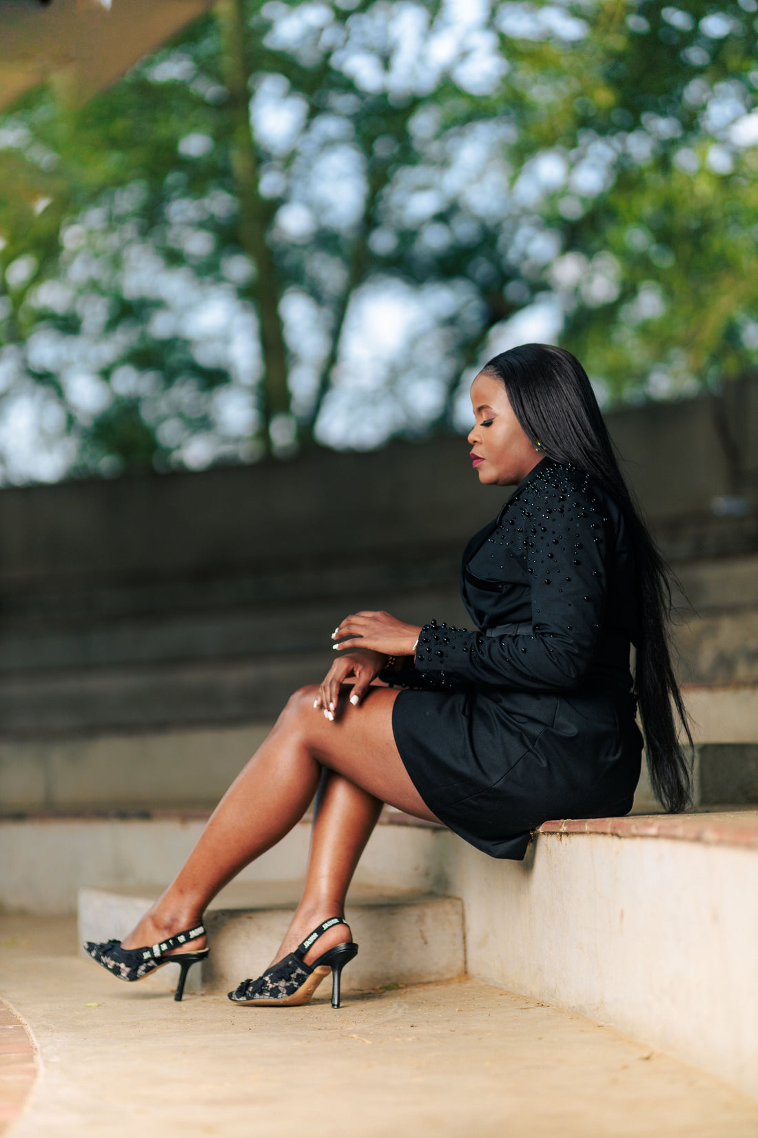 Woman in an elegant black dress sitting on outdoor steps in natural light, representing the timeless silhouette featured in CENT'ANNII's guide to the little black dress