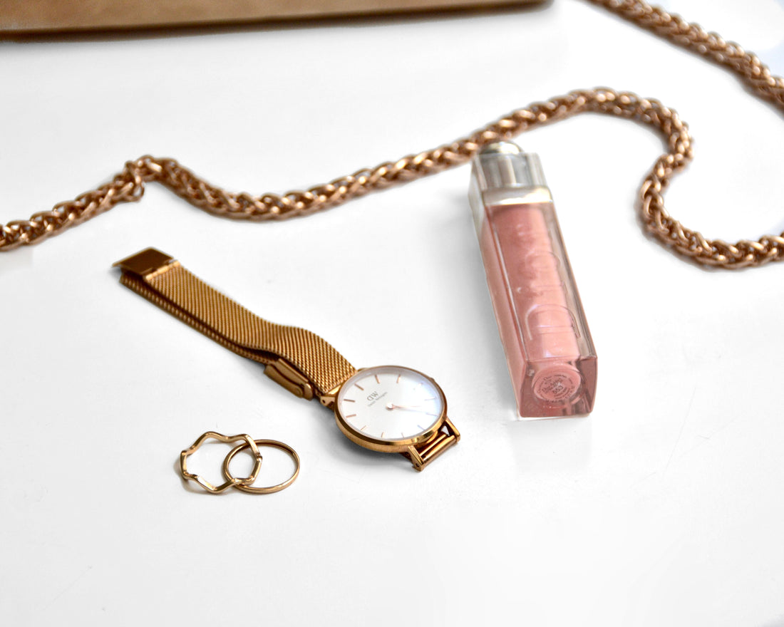 Gold wristwatch, rings, and chain necklace arranged in a flat lay on a white surface, evoking Michael Kors jet-set glamour