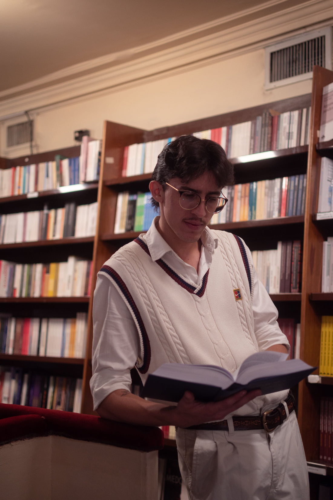 Young man in a tailored knit and trousers reading in an elegant, wood-paneled library, capturing the understated old money aesthetic