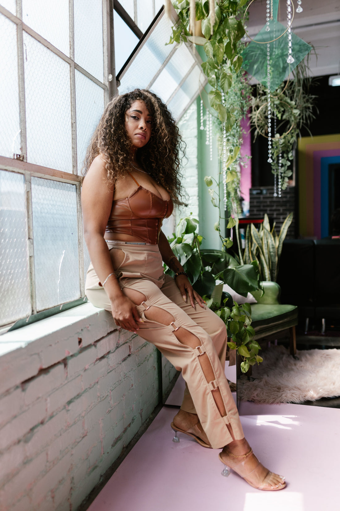 Confident plus size model styling a trendy pre-owned designer outfit indoors with a lush green backdrop