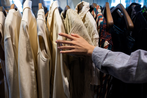 A shopper's hand examining the fabric texture of a pre-owned garment while considering a first-time purchase