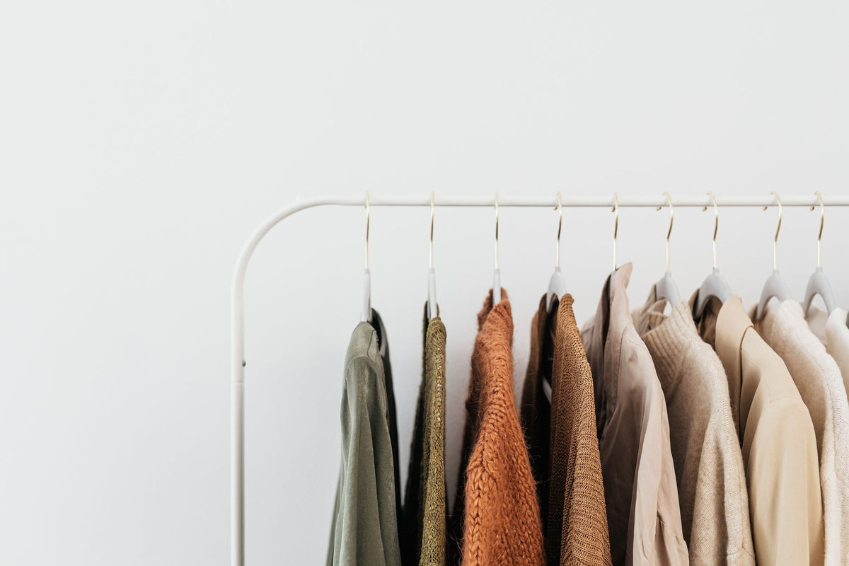 A minimalist clothing rack of neutral beige and brown-toned knitwear and jackets, representing the tonal wardrobe favored by quiet luxury designer brands