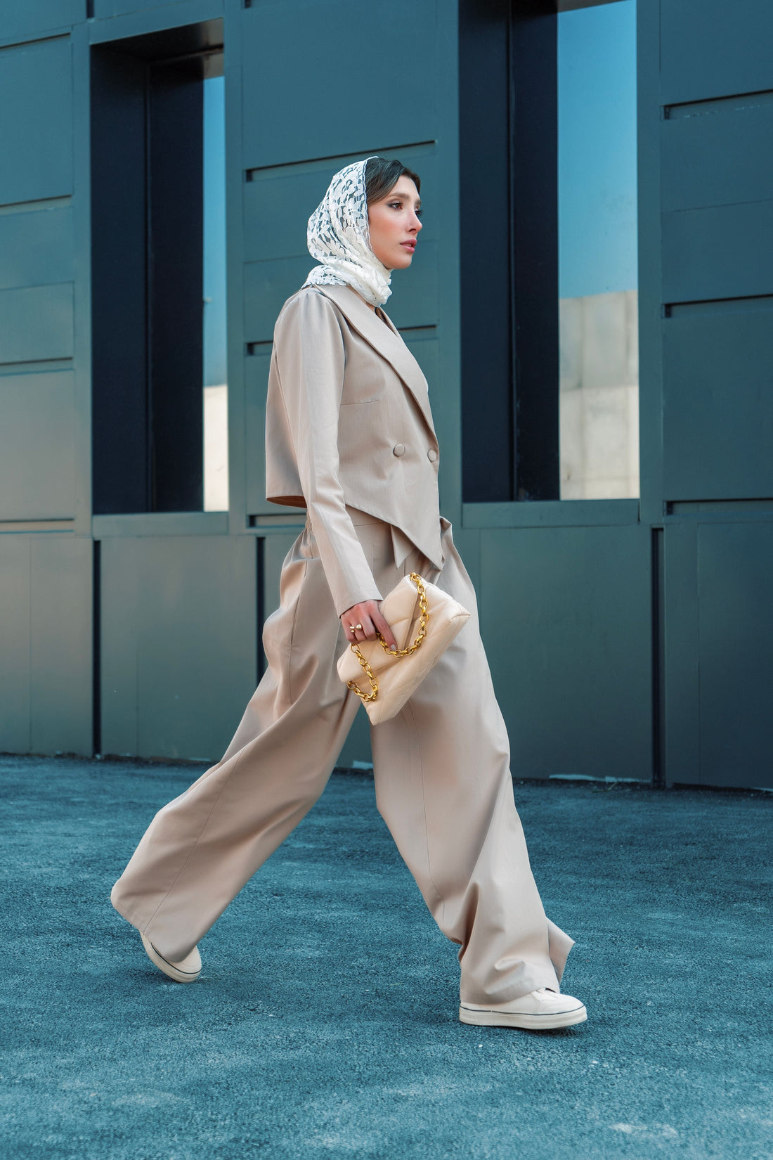 Elegant woman in a tailored beige suit walking past a modern building, embodying the neutral-toned, minimalist silhouette at the center of quiet luxury dressing