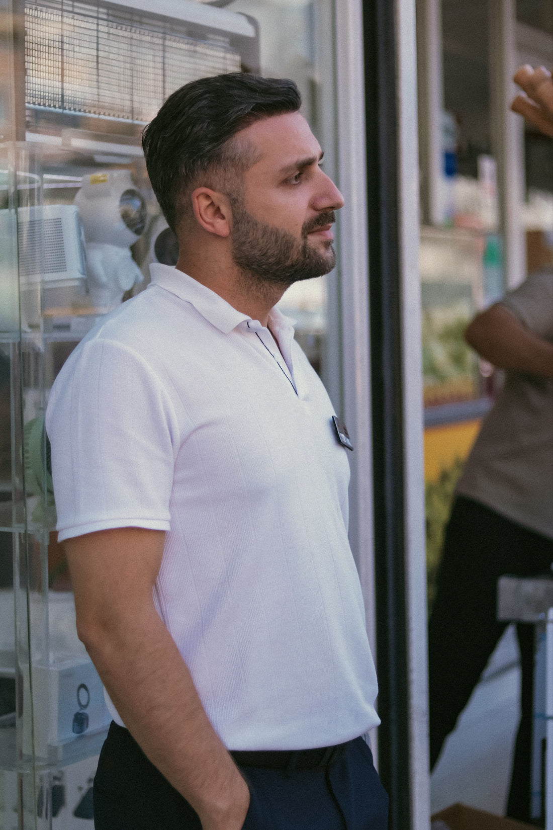 Man in a classic white polo shirt standing outside a storefront, representing the timeless Ralph Lauren polo silhouette