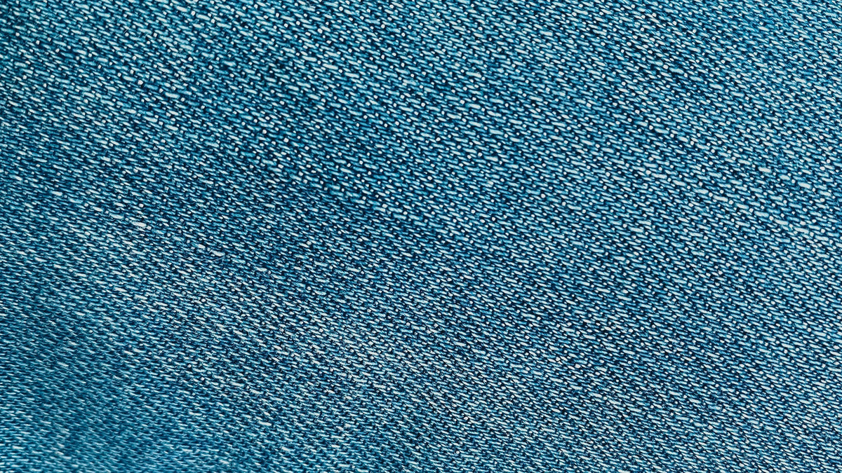 Macro close-up of raw indigo denim fabric showing its tight woven texture, illustrating the unwashed, unfaded surface characteristic of raw denim