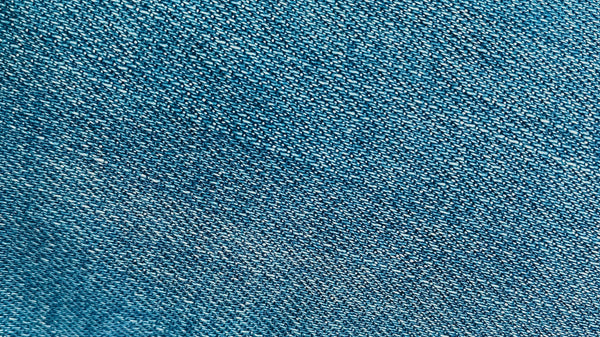 Macro close-up of raw indigo denim fabric showing its tight woven texture, illustrating the unwashed, unfaded surface characteristic of raw denim