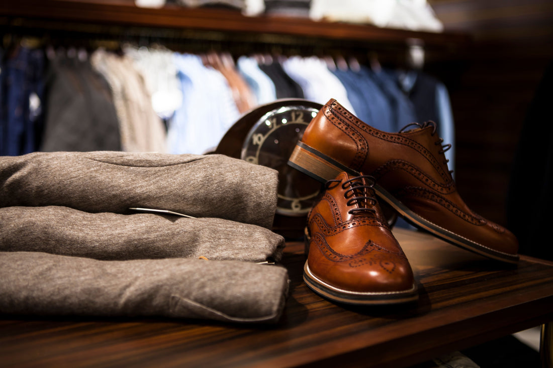 Brown leather wingtip shoes displayed alongside gray tailored clothing in a boutique setting