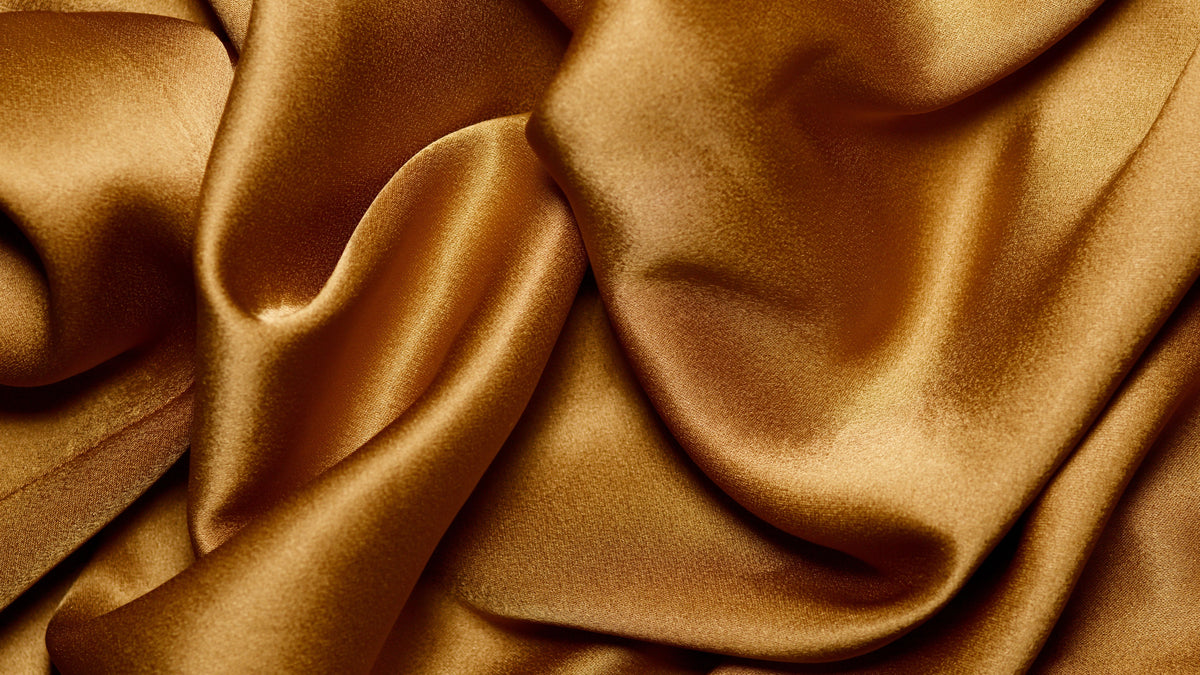 Close-up of smooth gold satin fabric with a soft, wavy sheen