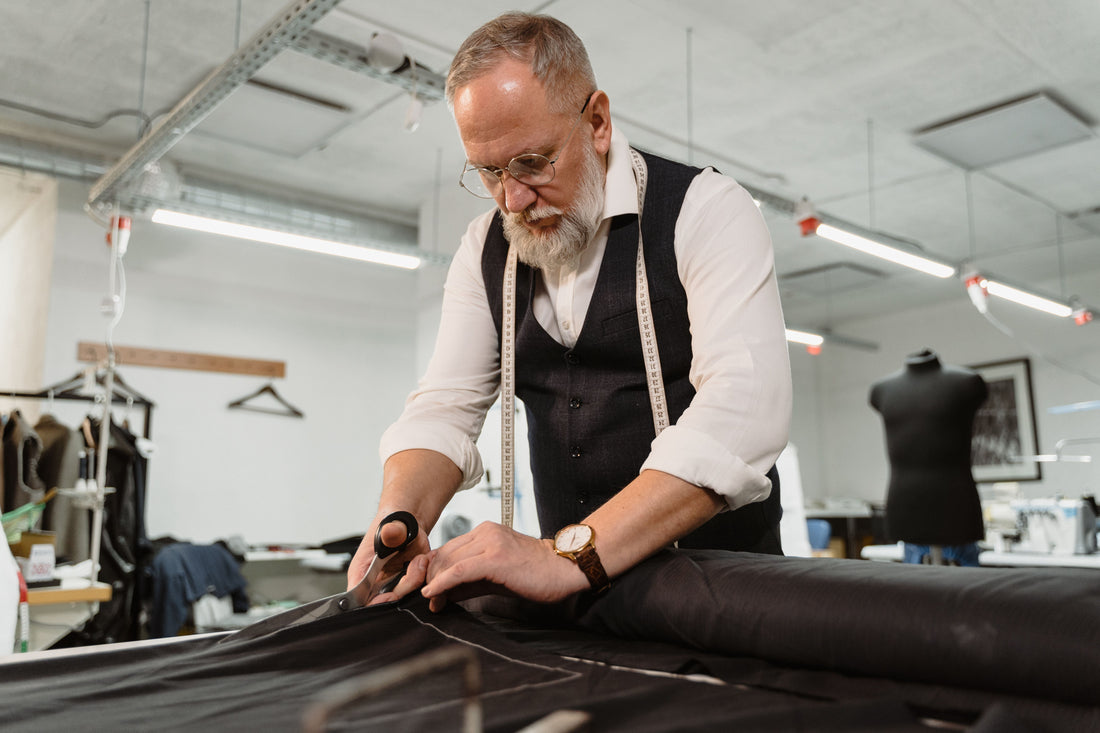 A senior tailor meticulously cutting fabric for a bespoke suit in a fashion studio