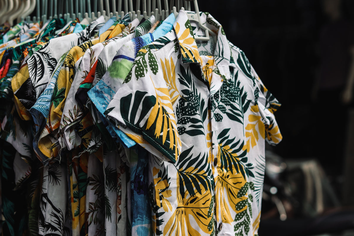 A rack of colorful tropical print camp shirts in a boutique, representing the resort-ready silhouettes collected in CENT'ANNII's guide to pre-owned Tommy Bahama
