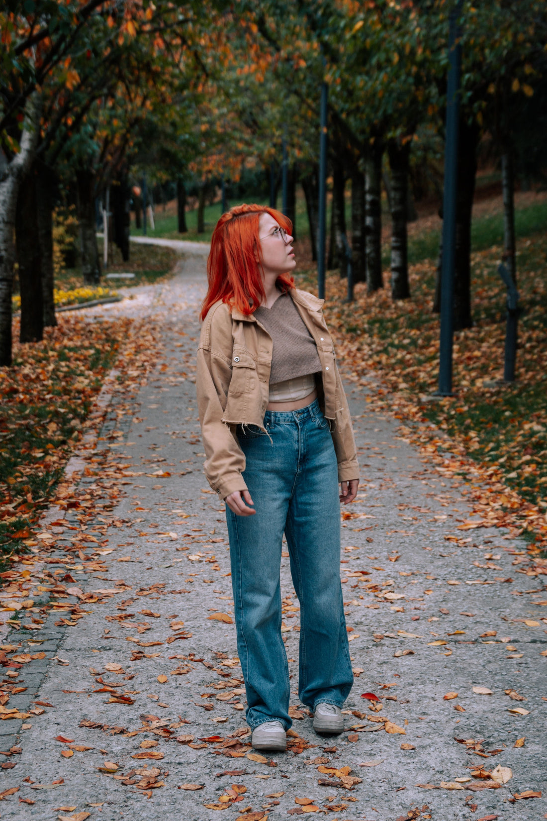 Woman in a denim jacket and jeans walking through a park in autumn, styling vintage denim for the season