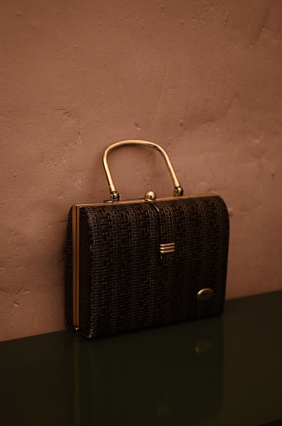 Classic vintage handbag with gold hardware against a textured wall, representing timeless pre-owned designer handbag design