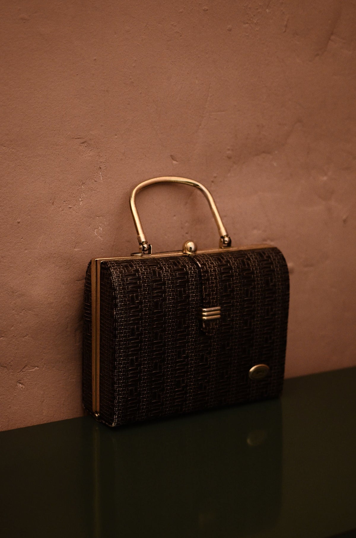 Classic vintage handbag with gold hardware against a textured wall, representing timeless pre-owned designer handbag design