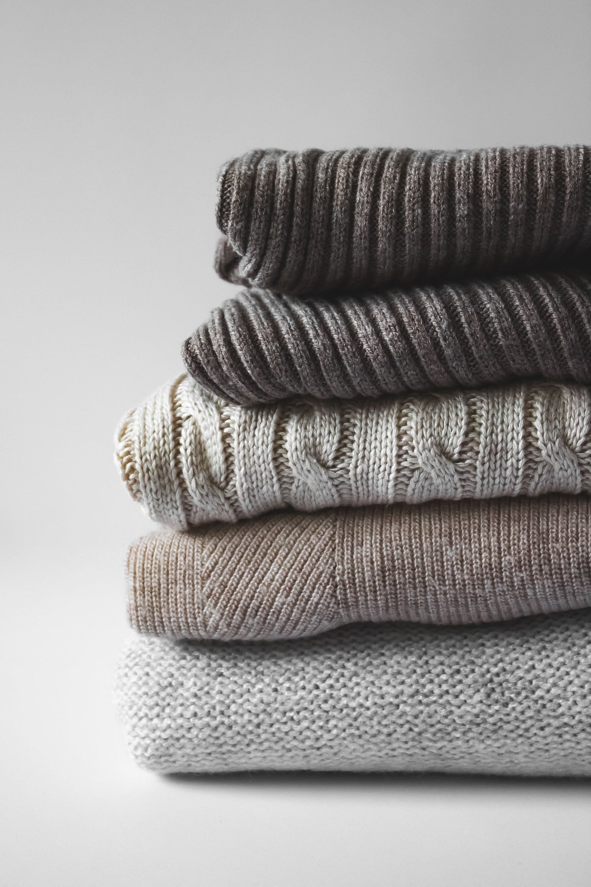 Neatly stacked pile of knitted wool sweaters in neutral tones, styled for a wool care guide