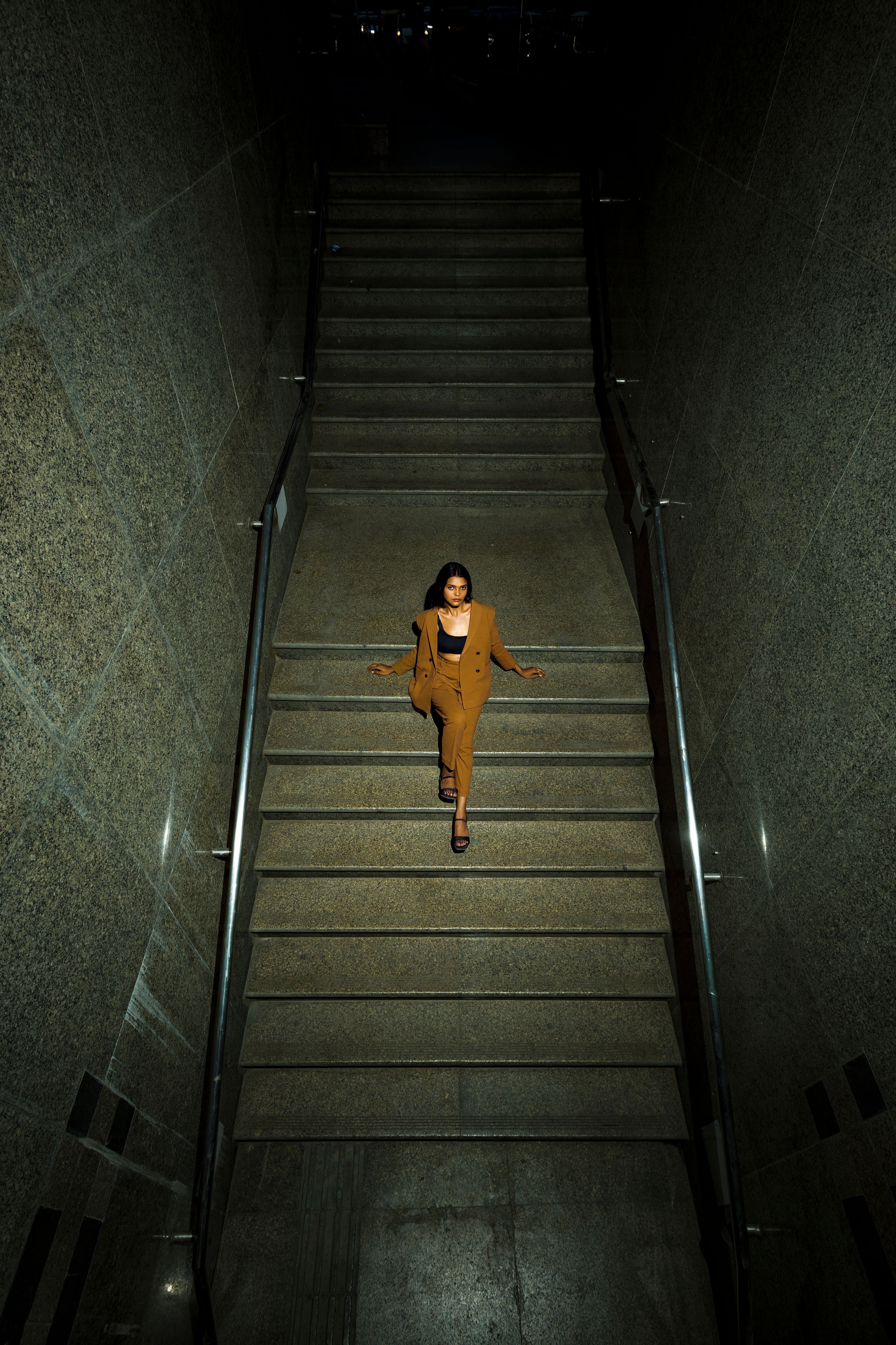 Woman in layered brown tones descending a dimly lit staircase, illustrating transitional seasonal dressing